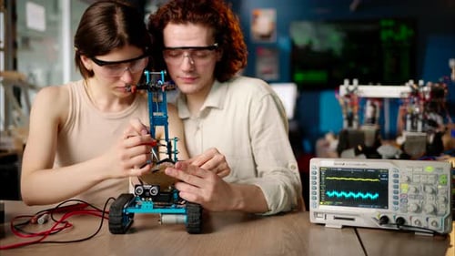 Two young happy engineers fixing a mechanical robot car in the workshop, using VR virtual reality he