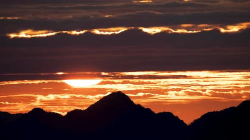 Silhouetten von Bergen bei goldenem Sonnenuntergang. Bewegliche Wolken am orangefarbenen Himmel.