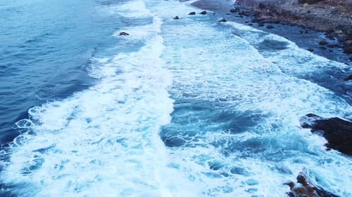 Birdseye Drone Shot of Cinematic Dark Rocks Coastline and Deep Blue Ocean Sea Water with Foamy White