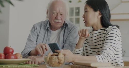 Woman and Senior Man Laughing While Watching Smartphone