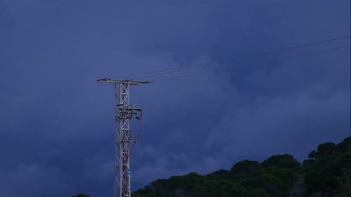 Cloudscape at sundown over a forested hillside with an electrical transmission tower in the foregrou