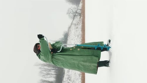 Fischer bohrt beim Winterfischen Eis auf einem gefrorenen See. Vertikales Video