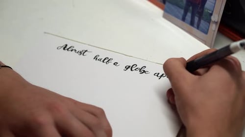 A Person Writes In The Calligraphic Handwriting In A White Paper. Close up