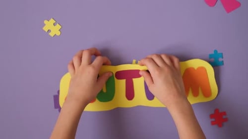 The child places a yellow card with multicolored letters forming the word autism