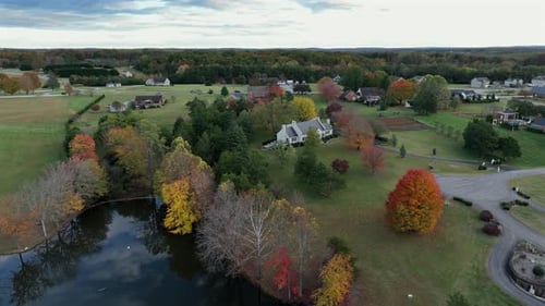 Mansion with private lake and colored trees in fall season. Quiet suburbia of american town. Aerial