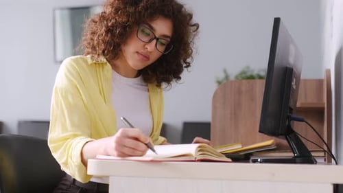Recherchieren von Informationen, mit Notizblock und Stift. Die Frau ist in der Bibliothek mit Computern.
