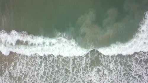 Stormy sea with waves breaking, white foam and beach sand dragged into the sea