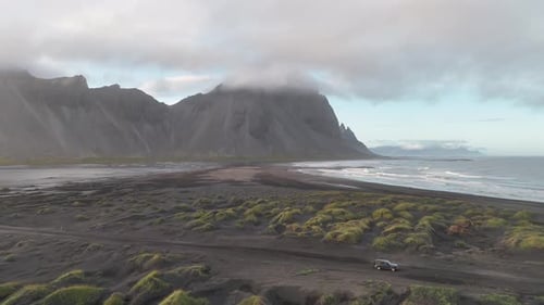 Vue aérienne large révélant une seule voiture garée dans les vastes paysages de Stokksnes, en Islande, sur le s
