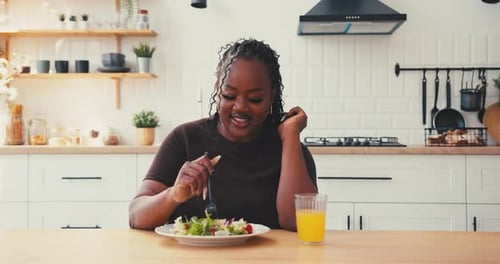 Curvy Black Woman Eats Fresh Green Salad Drinking Orange Juice