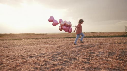 Little Happy Boy Running With HeartShaped Balloons On Sky Background On Field