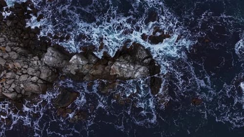 Waves crash on rocky shoreline near ocean in bright daylight