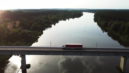 Lorry and trailer driving over a bridge over a river in time for sunset in the sunlight.