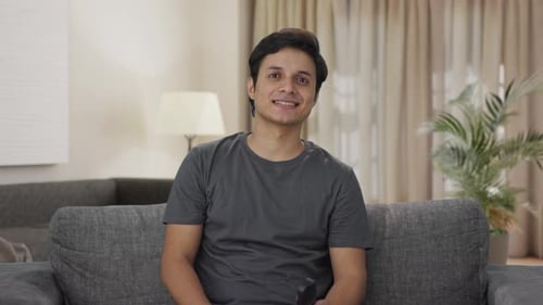 Smiling Man Sitting on Sofa Using Remote