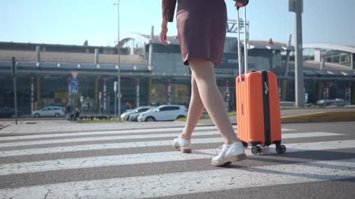 Mulher andando com mala laranja na faixa de pedestres fora do terminal do aeroporto