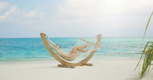 Idyllic Scene. Beautiful Woman Sunbathing Lying in Hammock on a Beach. Azure Beach with White Sands