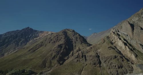Cinematic drone aerial of a rugged mountain slopes and rocky ridges under clear blue sky, revealing