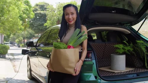 Retrato de una mujer asiática después de comprar alimentos en un coche eléctrico
