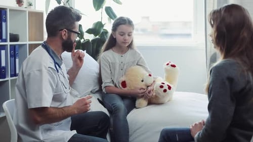 Médico caucásico con gafas habla sobre el estado de salud satisfactorio de la niña después de un examen