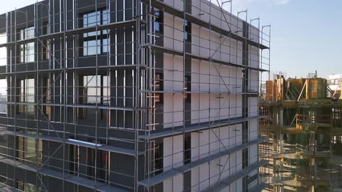 Construcción de un edificio moderno de varios pisos con andamios en una zona urbana concurrida al atardecer