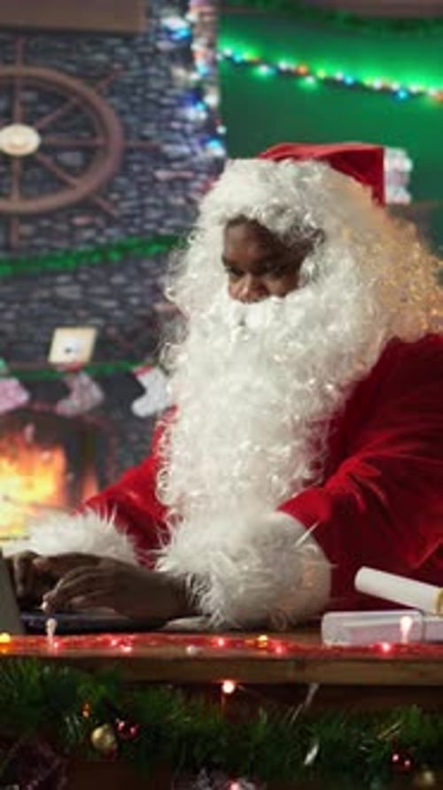 Vertical Video Santa Claus Uses a Laptop in His Festive Log Cabin Navigating Online Webpages