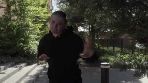 A dancer performs a light-hearted freestyle hip-hop routine on a city sidewalk.