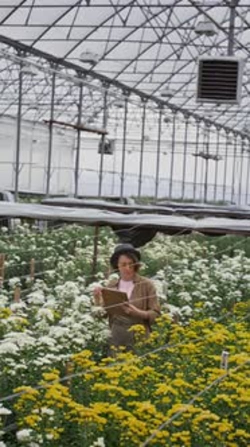 Woman Inspecting Flowers in Greenhouse With Clipboard