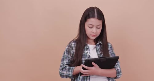 Schoolgirl using computer tablet to study and take notes on brown background