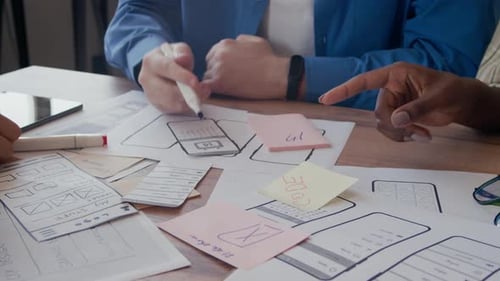 UX Designers Writing on Papers at Desk Discussing Mobile Interface Mockup