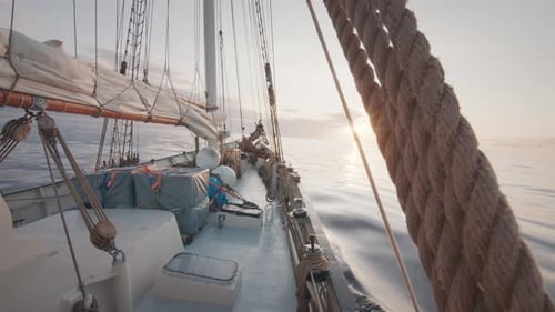 Sailing vessel moves in the calm glassy open sea with sun rising on the horizon