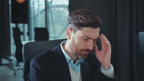 Un jeune homme d'affaires épuisé utilise un ordinateur et ressent des maux de tête, une dépression, un travail bouleversé dans un bureau moderne