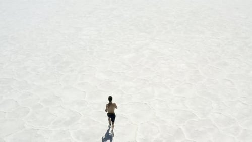 Drone footage of a man running on salt flats in Death Valley, California.