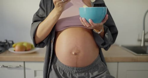 Pregnant Woman Eating Fruit in Kitchen
