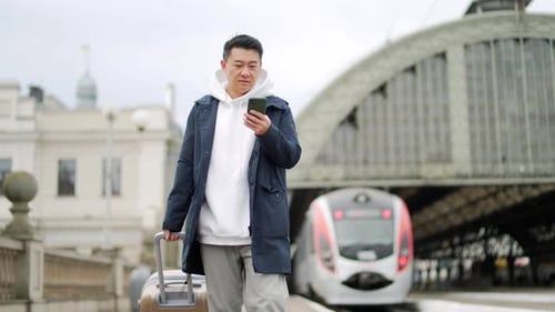 Man With Suitcase Using Smartphone at Train Station
