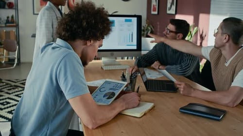Man Making Notes, Looking at Tablet and Listening to Presentation in Office