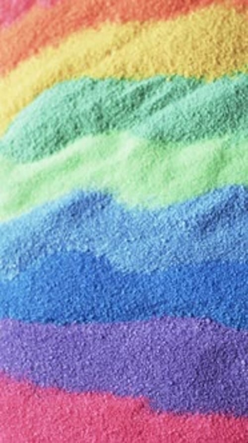Vertical video of close up of rainbow coloured sand grains and copy space background