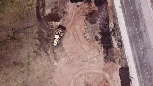 following a yellow frontal loader carrying black dirt over to excavator. driving trough a constructi