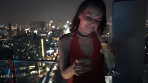 Woman Texting on Smartphone and Drinking Beverage on Terrace in Bar At