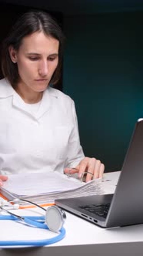 Vidéo verticale femme médecin lisant des dossiers médicaux sur un bureau avec ordinateur portable et stéthoscope