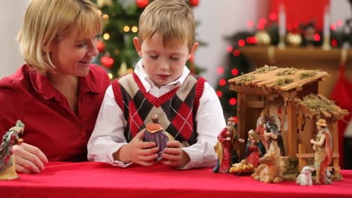Boy and Woman Arrange Christmas Nativity Scene Figures