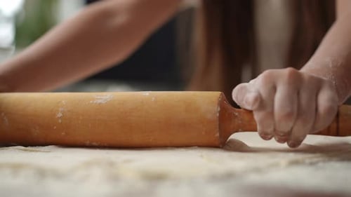 Closeup A Girl is Trying to Roll Out Dough on the Table Using a Rolling Pin