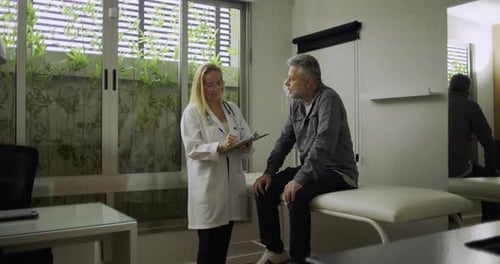 Female Doctor Taking Notes Talking with Male Patient