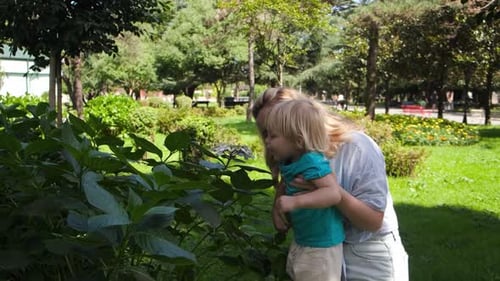 Kind im Arm der Mutter schnüffelt Blumen im Park