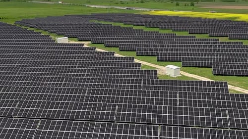 Expansive solar panel farm in a green field under a clear sky, aerial view