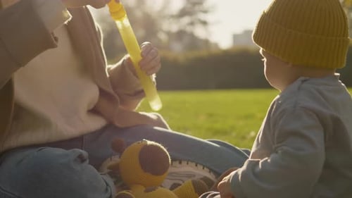 Mother and child enjoy blowing bubbles together in a sunny park