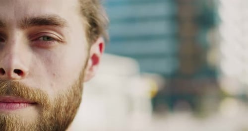 Nahaufnahme einer Hälfte des männlichen Gesichts mit Bart und Haaren im Schwanz im Freien mit offenen Augen, gut aussehend, jung