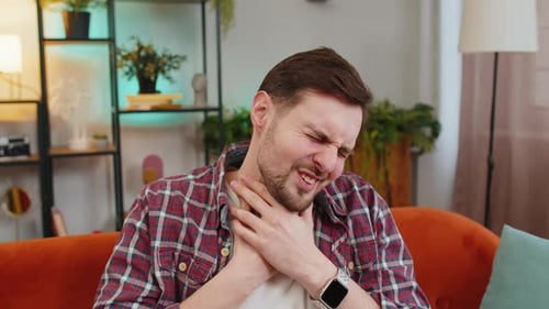 Man Gripping Sore Throat in an Indoor Setting
