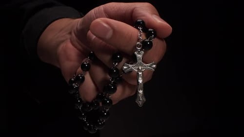Hand Holding a Black Rosary with Silver Cross
