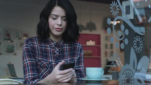 Mujer adulta joven mirando un teléfono inteligente en un café
