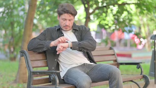 Man Checking Smartwatch While Sitting on Bench