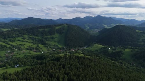Aerial View of Green Mountain Valley with Forest Hills and Distant Peaks Under Clouds
